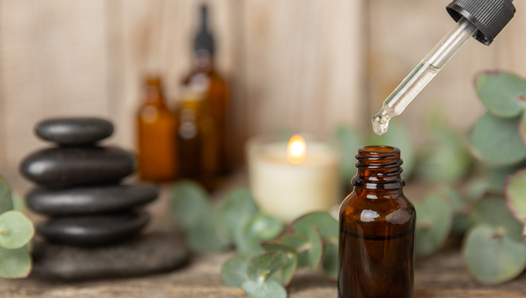 A dropper hanging out an essential oil bottle with a serene spa background