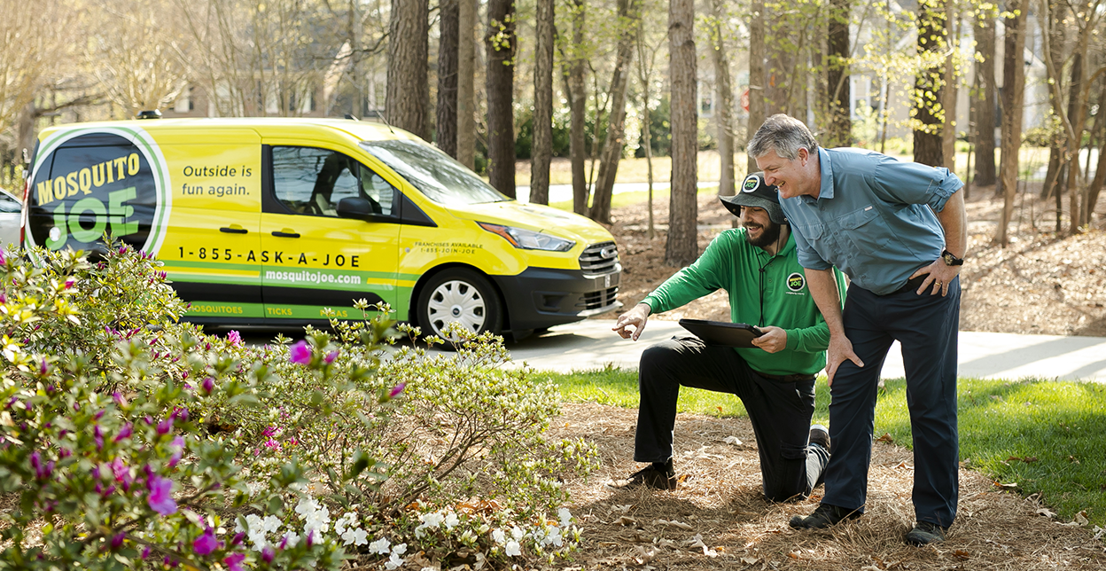 A Mosquito Joe employee pointing at plants with a customer in front of a van.